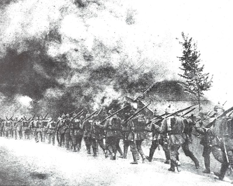 A column of German troops march through a burning Belgian village. 